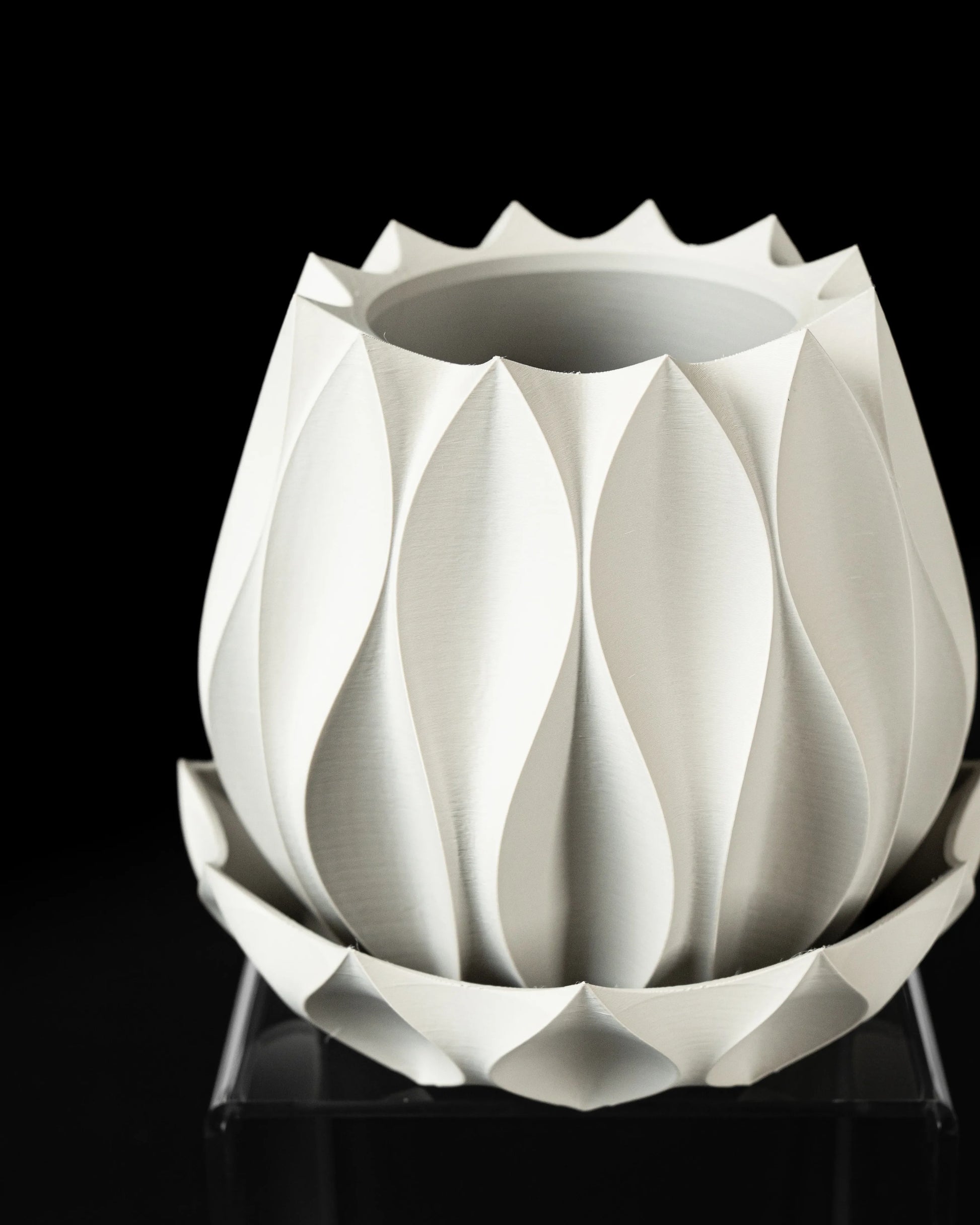 Pot décoratif blanc mat en matériau moderne, formes géométriques en relief rappelant des feuilles stylisées, posé sur une.