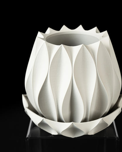 Pot décoratif blanc mat en matériau moderne, formes géométriques en relief rappelant des feuilles stylisées, posé sur une.