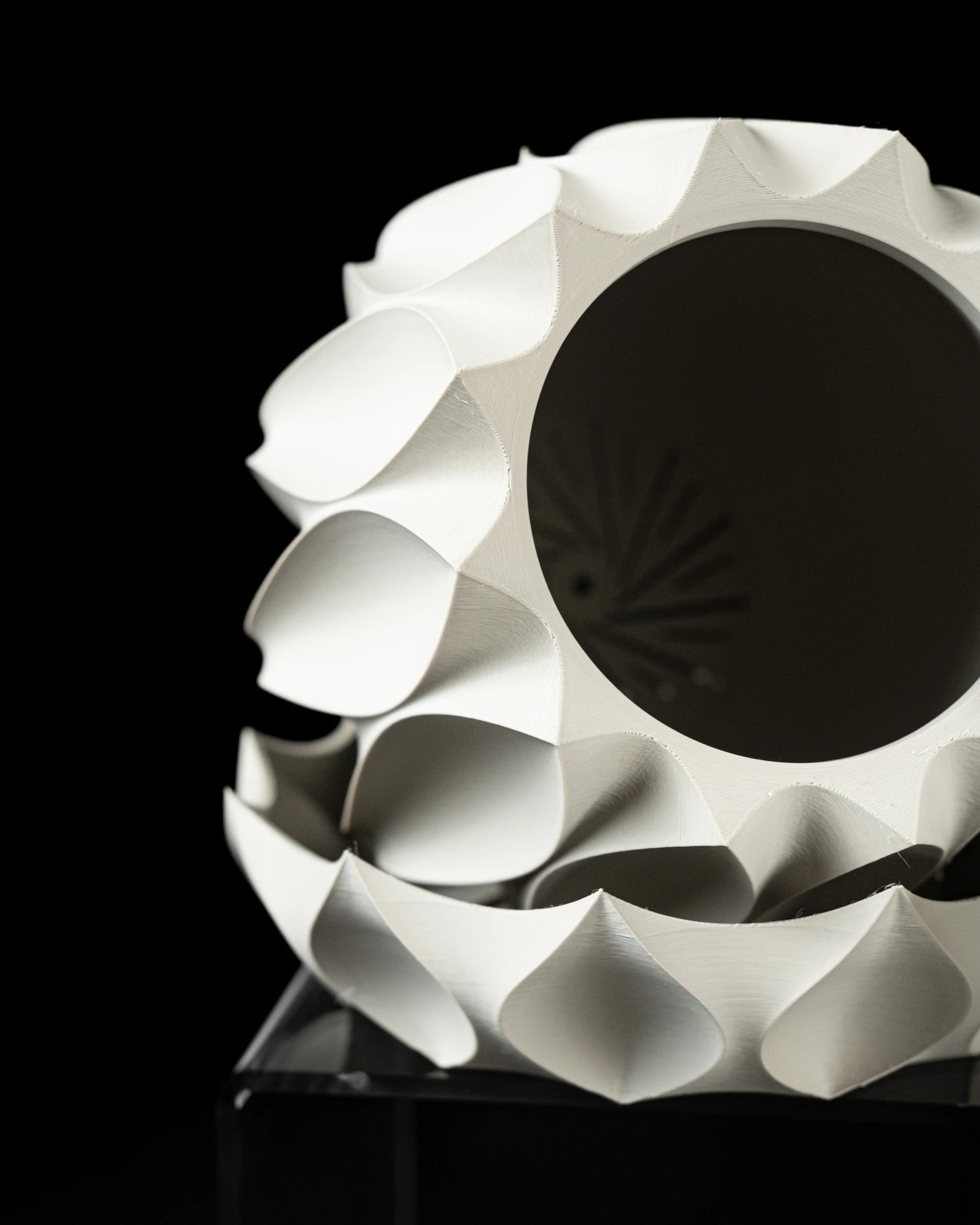 Pot décoratif blanc en forme sphérique avec motifs ondulés en relief et ouverture circulaire noire au centre, design moderne