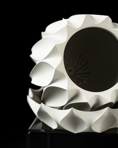 Pot décoratif blanc en forme sphérique avec motifs ondulés en relief et ouverture circulaire noire au centre, design moderne