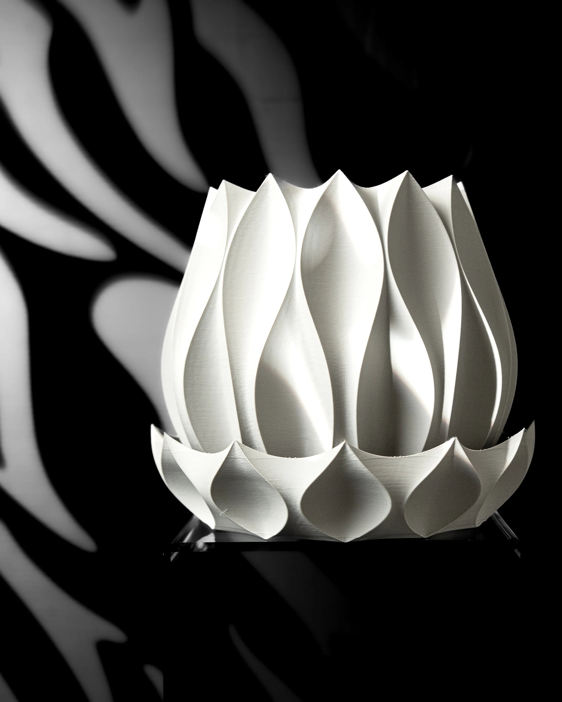 Pot décoratif blanc mat en forme de pétales incurvés superposés, style moderne et sculptural, posé sur fond sombre avec.