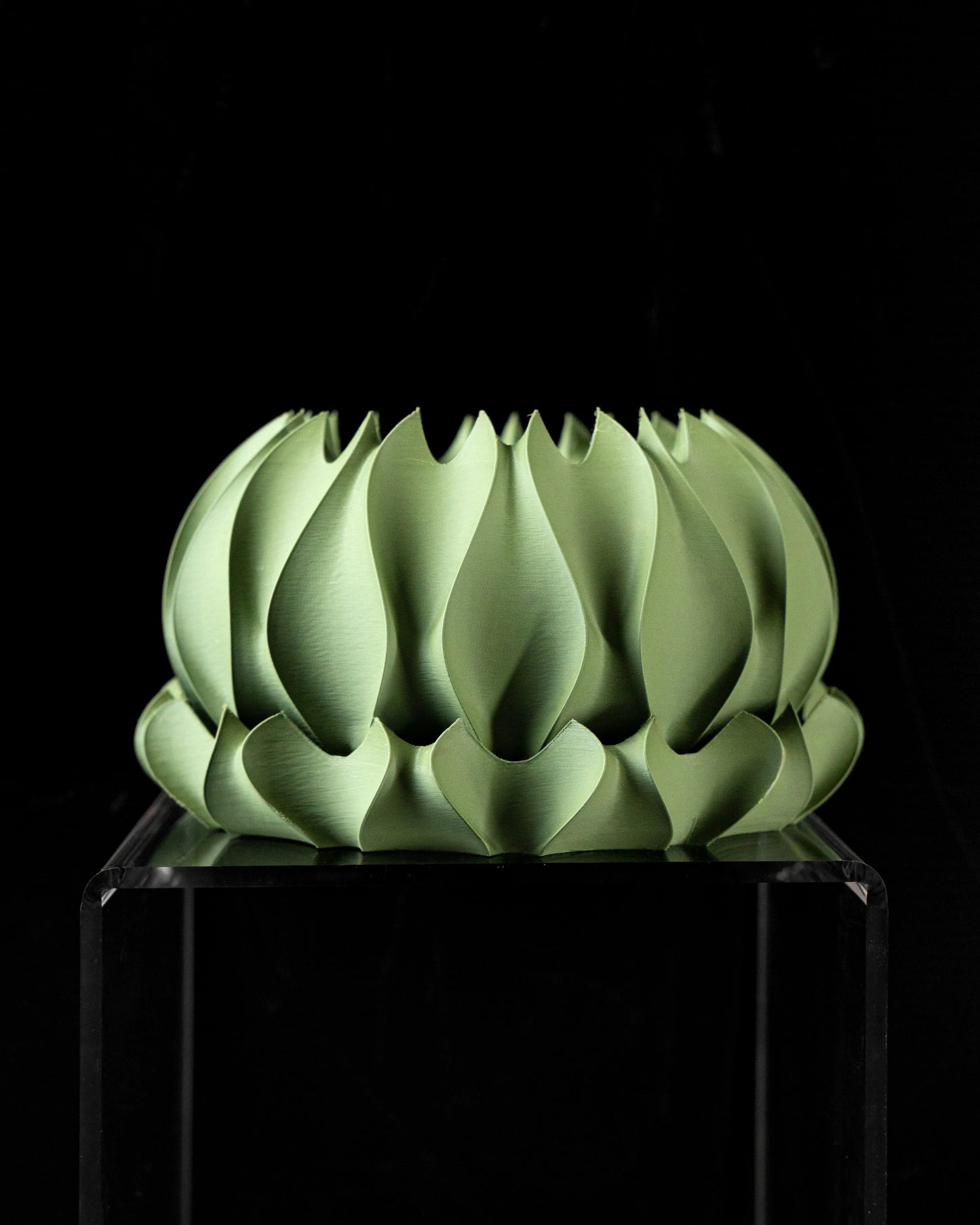 Pot décoratif vert pâle en forme de feuilles stylisées entrelacées, aux contours sculptés et texture lisse, posé sur un.