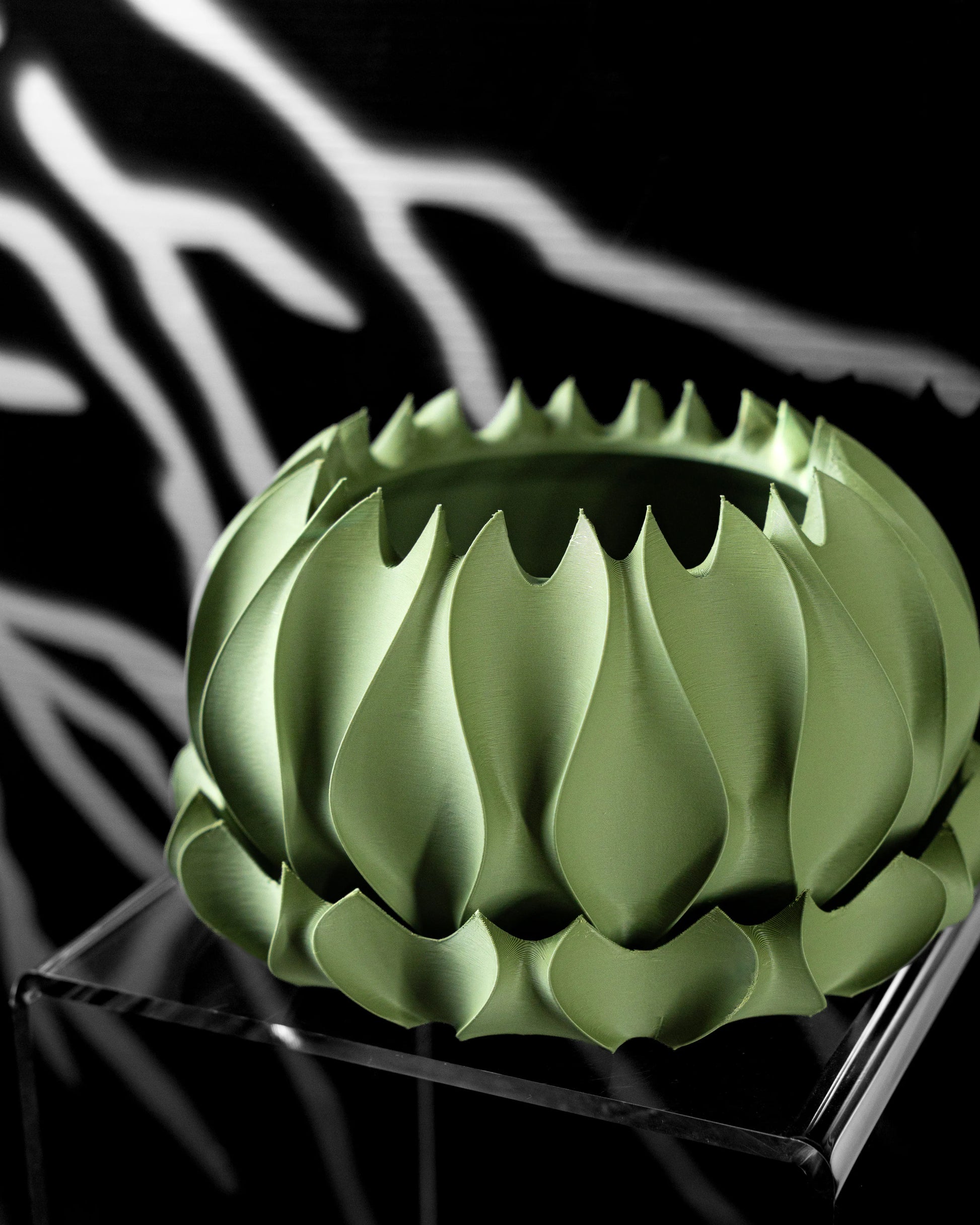 Pot décoratif vert sauge en matière mate, avec motif ondulé et bords irréguliers en dents de scie, posé sur socle noir.