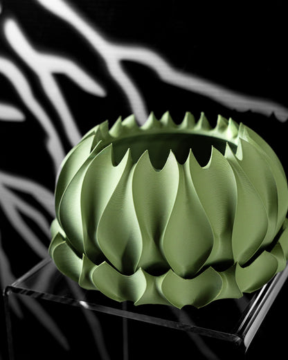 Pot décoratif vert sauge en matière mate, avec motif ondulé et bords irréguliers en dents de scie, posé sur socle noir.