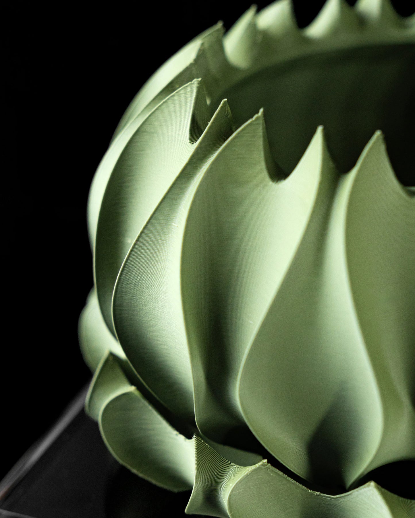 Pot décoratif vert mousse en forme de spirale avec surfaces lisses et découpes dentelées, design moderne et sculptural.