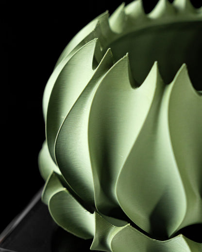 Pot décoratif vert mousse en forme de spirale avec surfaces lisses et découpes dentelées, design moderne et sculptural.