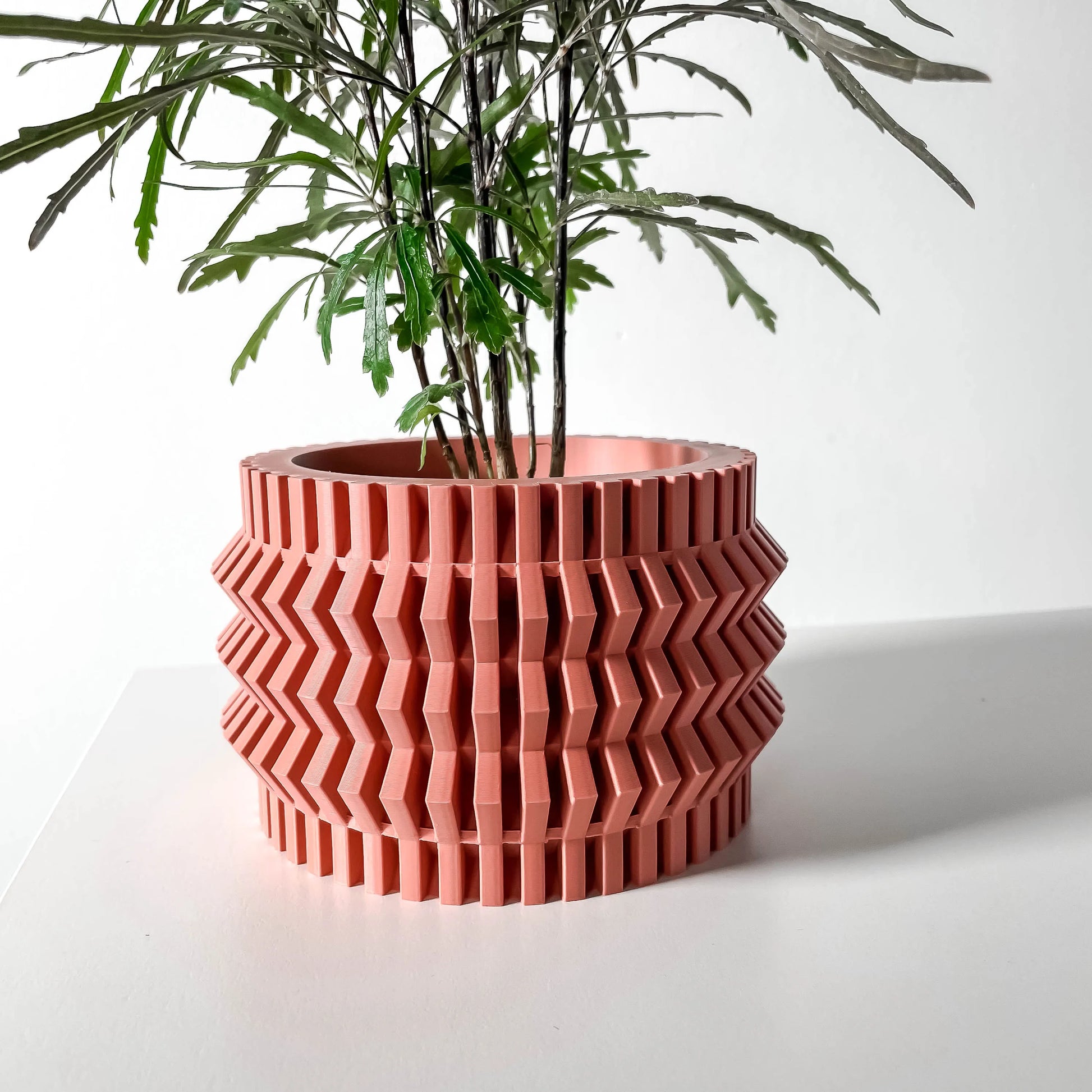 Pot décoratif moderne terracotta en matière texturée avec motifs géométriques en zigzag, plante verte à fines feuilles.