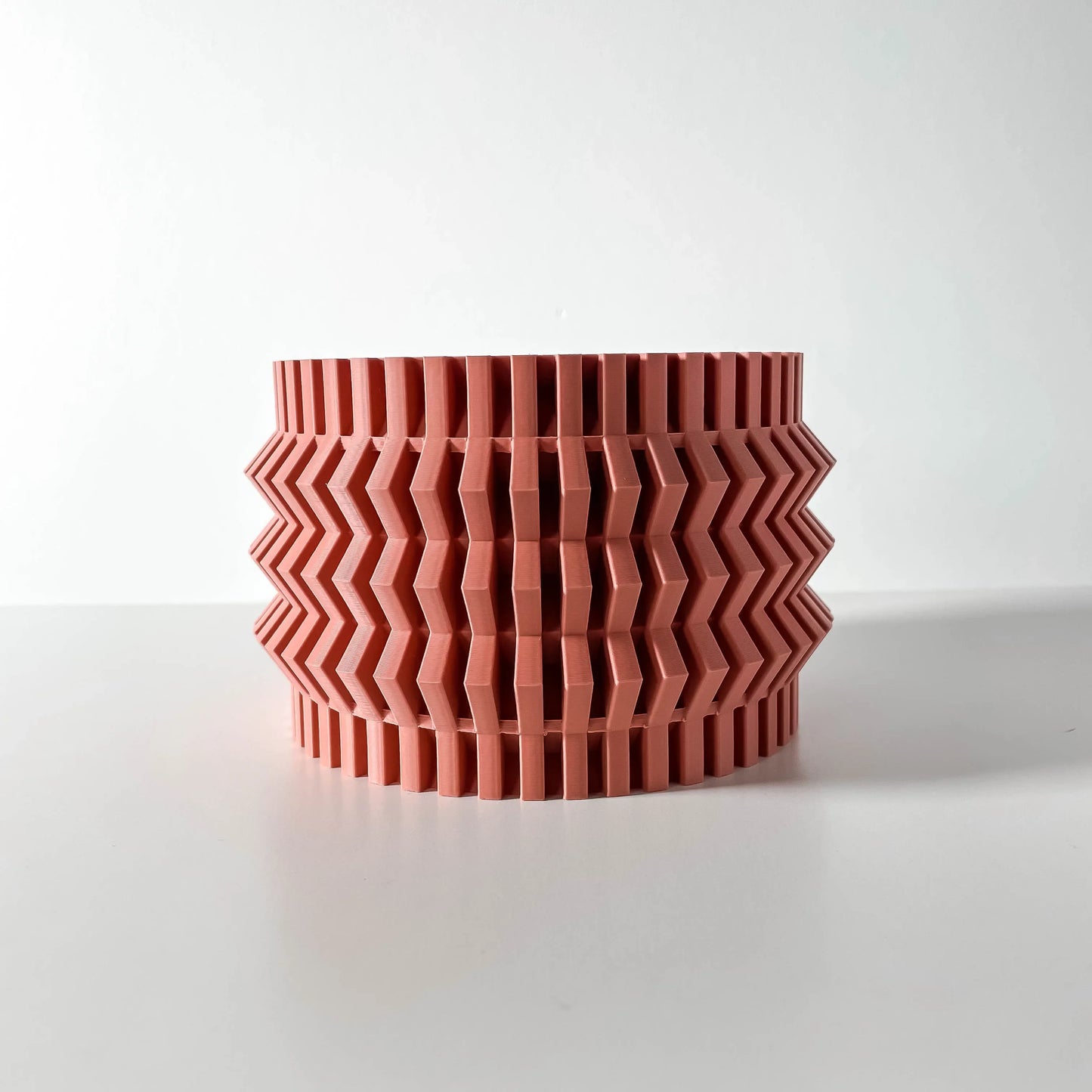 Pot décoratif Alio cylindrique en plastique rouge brique avec motifs en zigzag en relief formant une texture géométrique.