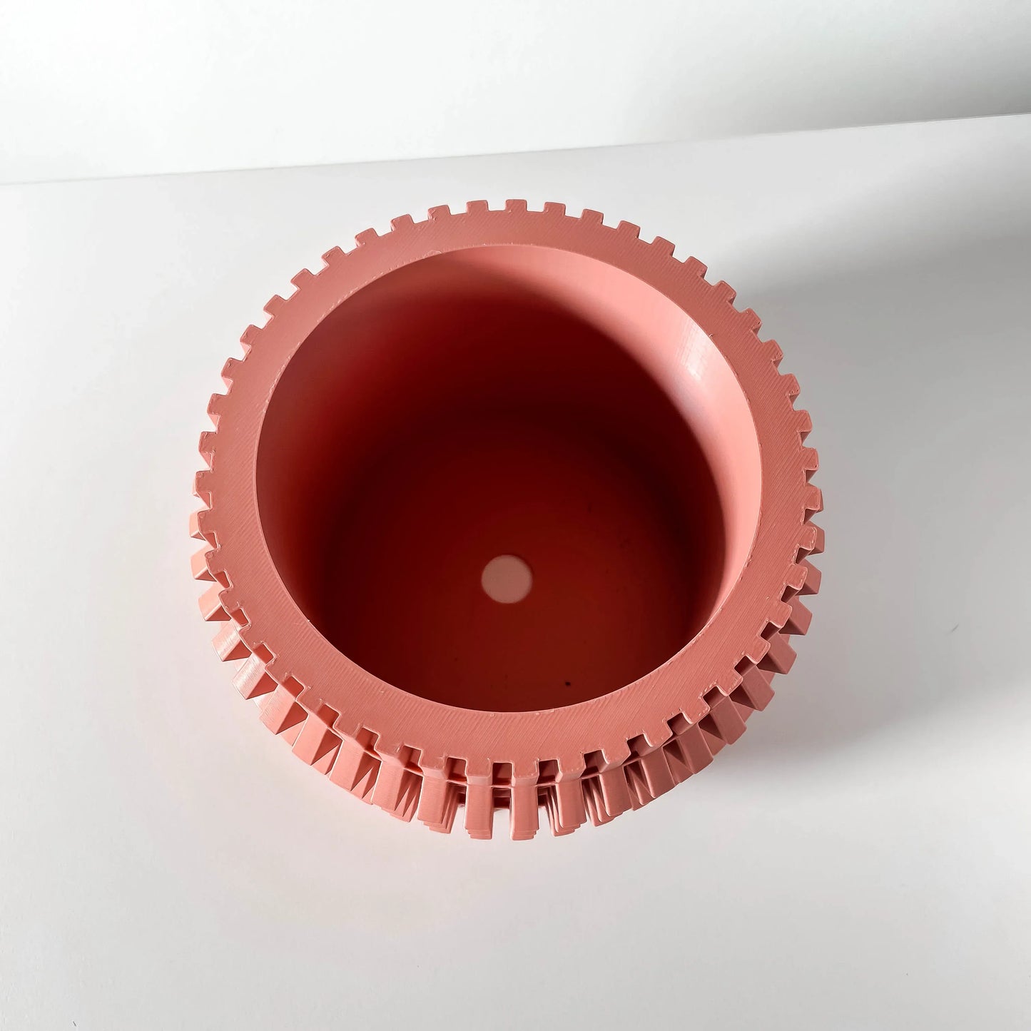 Pot décoratif rond rose avec bord cranté évoquant un engrenage, intérieur lisse, style moderne minimaliste.