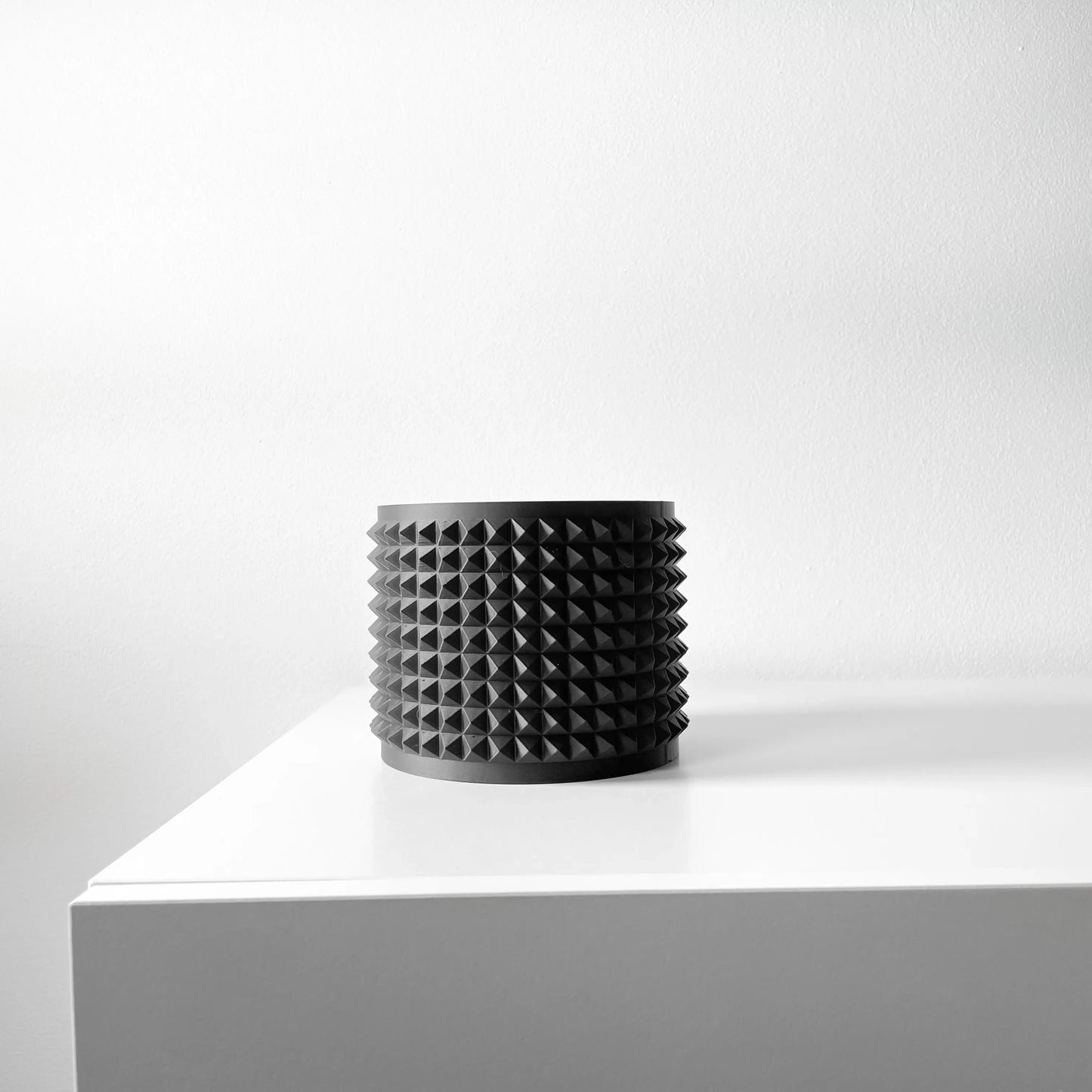 Pot décoratif noir mat cylindrique orné de picots réguliers en relief sur toute la surface, style moderne, posé sur une.