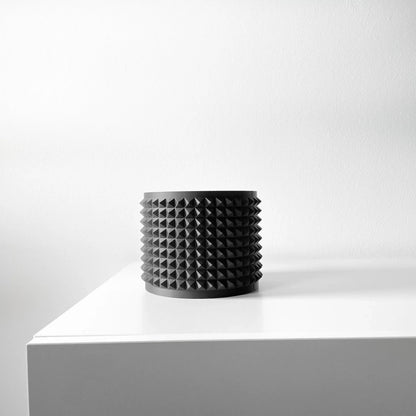 Pot décoratif noir mat cylindrique orné de picots réguliers en relief sur toute la surface, style moderne, posé sur une.