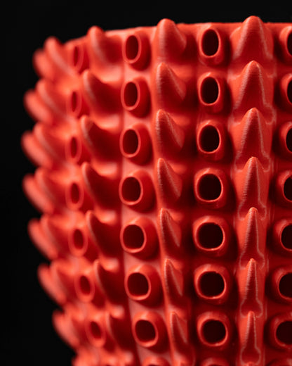 Pot décoratif rouge vif avec texture tubulaire en relief rappelant des branches de corail, surface mate et structure moderne.