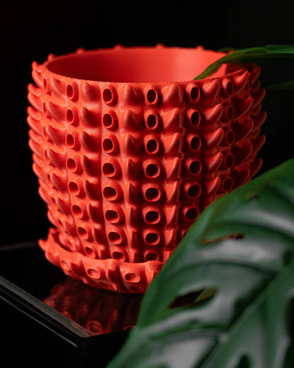 Pot décoratif rouge vif avec texture en relief formée de rangées de petites excroissances cylindriques, style moderne et.