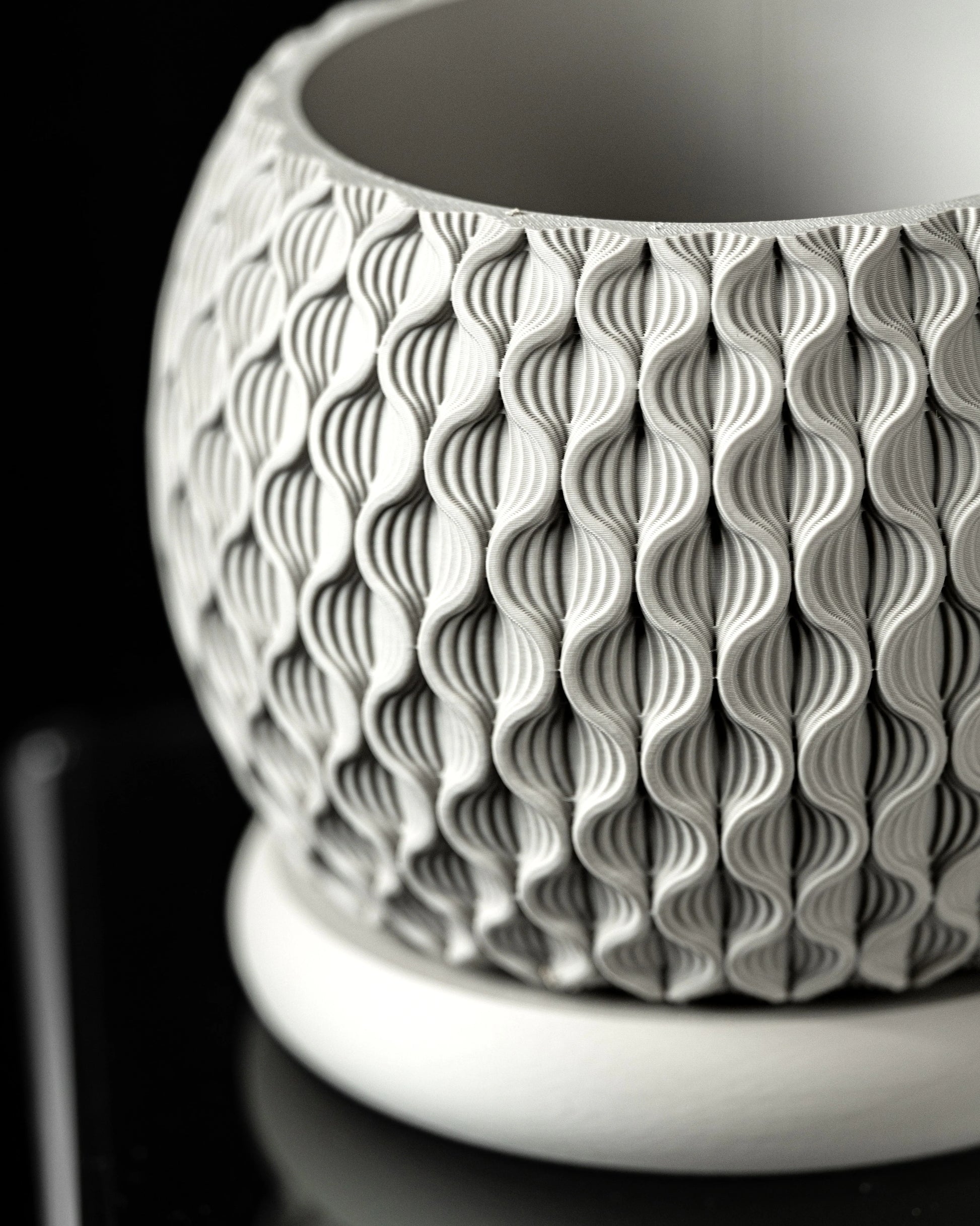 Pot décoratif blanc en matériau moderne avec surface texturée en motifs ondulés verticaux, forme arrondie avec base plate.