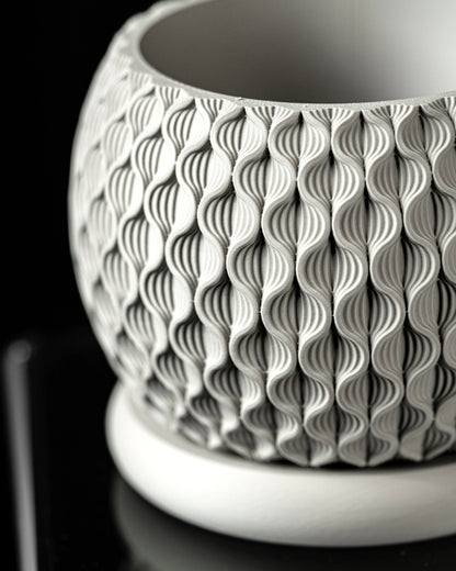 Pot décoratif blanc en matériau moderne avec surface texturée en motifs ondulés verticaux, forme arrondie avec base plate.