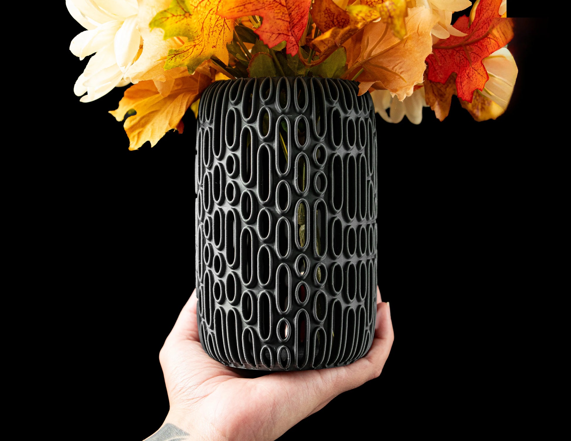 Vase noir mat à motifs géométriques ovales en relief, forme cylindrique, rempli de fleurs séchées orange, jaune et crème,.