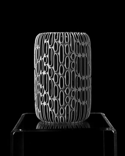 Vase cylindrique noir mat avec motifs ovales creux allongés en relief blanc, design moderne et graphique.