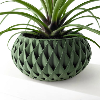 Pot décoratif vert foncé avec motif géométrique en relief, forme ronde et large, accueillant une plante verte aux feuilles.