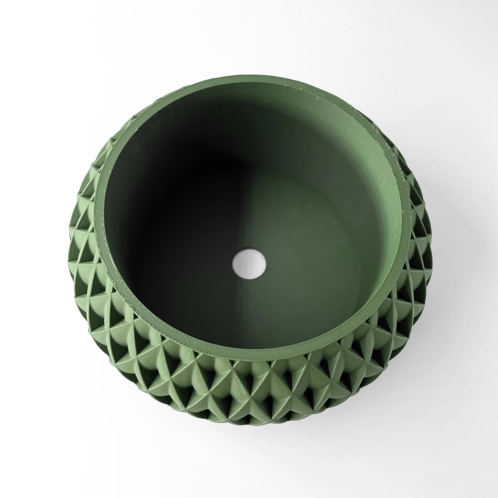 Pot décoratif vert foncé en plastique avec surface extérieure à motif géométrique en relief, forme ronde avec ouverture.