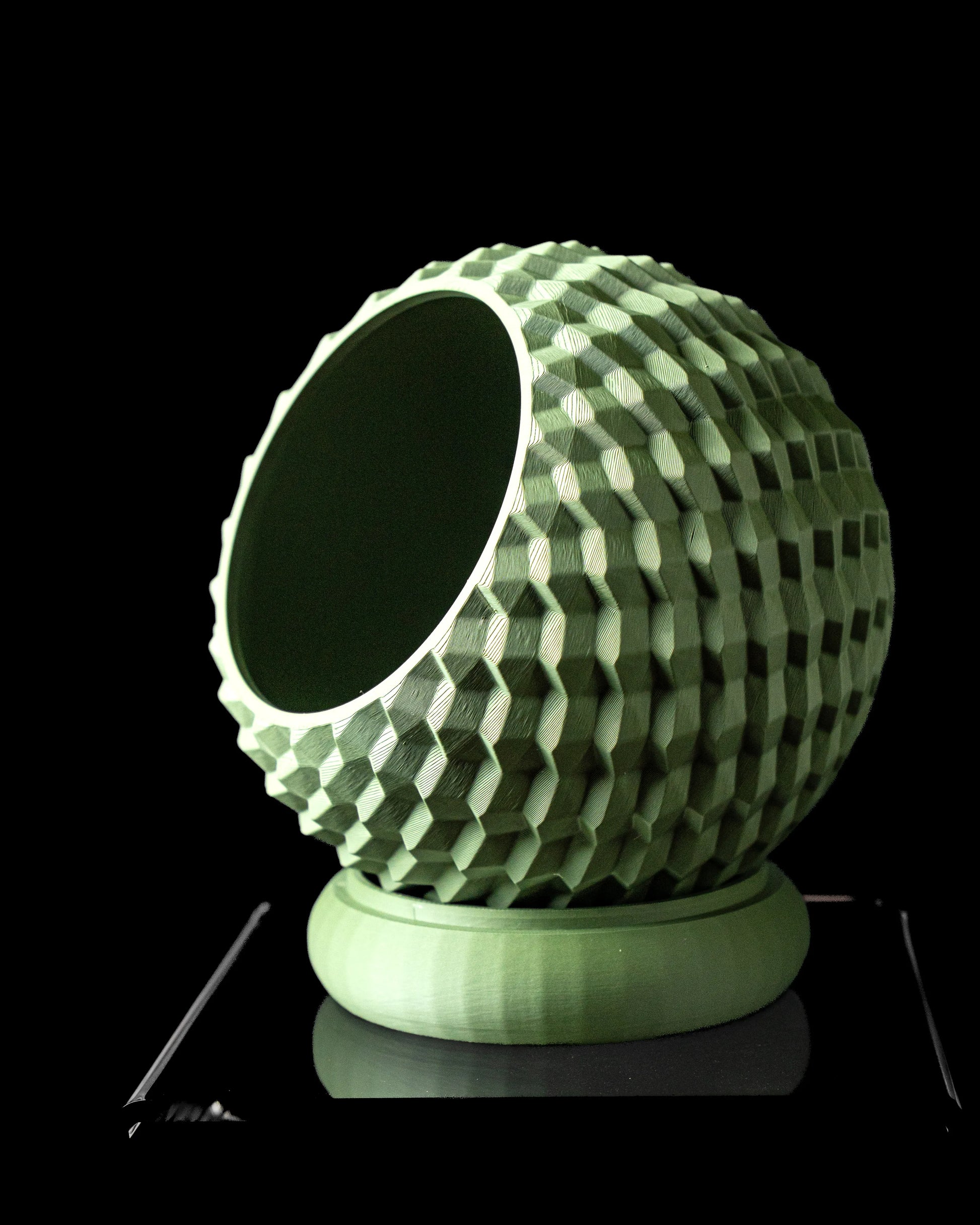 Pot décoratif vert pâle aux motifs géométriques en relief, forme sphérique inclinée, socle circulaire assorti.