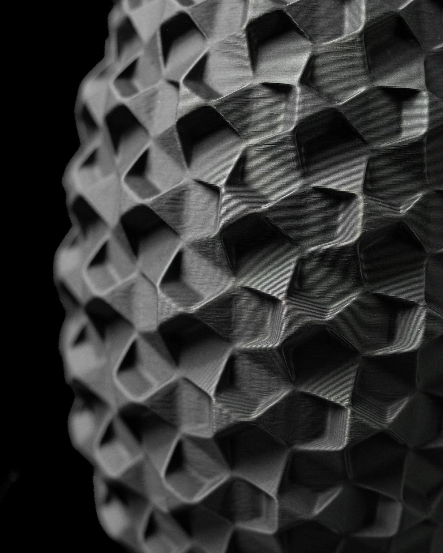 Vase noir mat à surface géométrique en relief, motif facetté moderne et profond, forme cylindrique allongée.