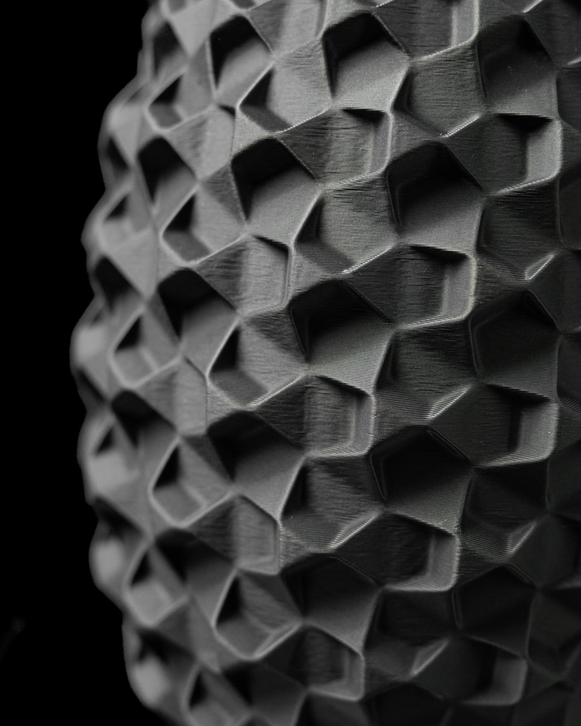 Vase noir mat à surface géométrique en relief, motif facetté moderne et profond, forme cylindrique allongée.