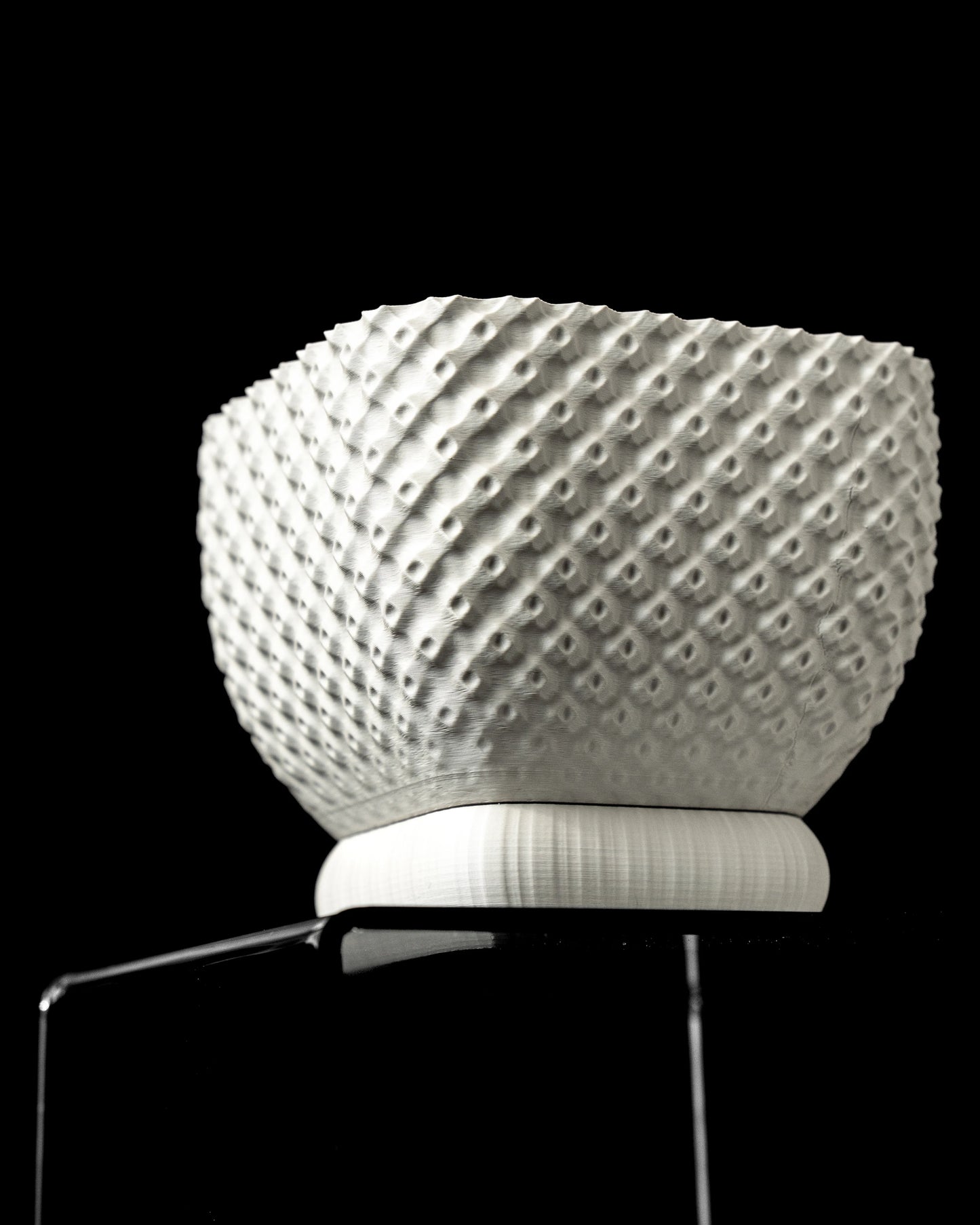 Pot décoratif blanc en matière texturée à motifs géométriques en relief, forme arrondie et base plate sur un support.