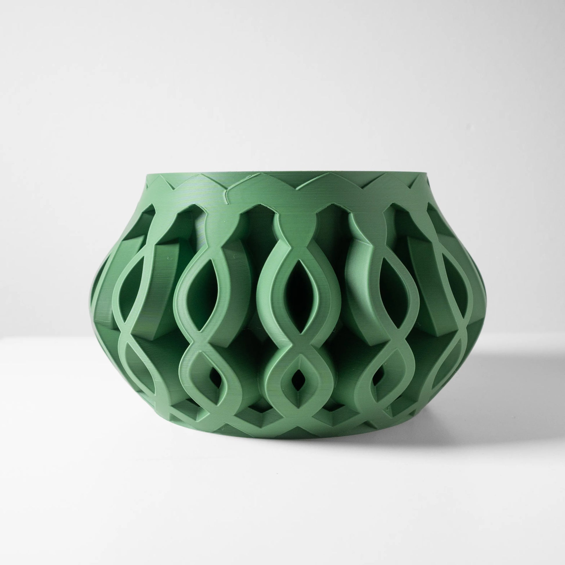 Pot décoratif vert mousse en plastique avec motifs géométriques entrelacés en relief, forme arrondie évasée.