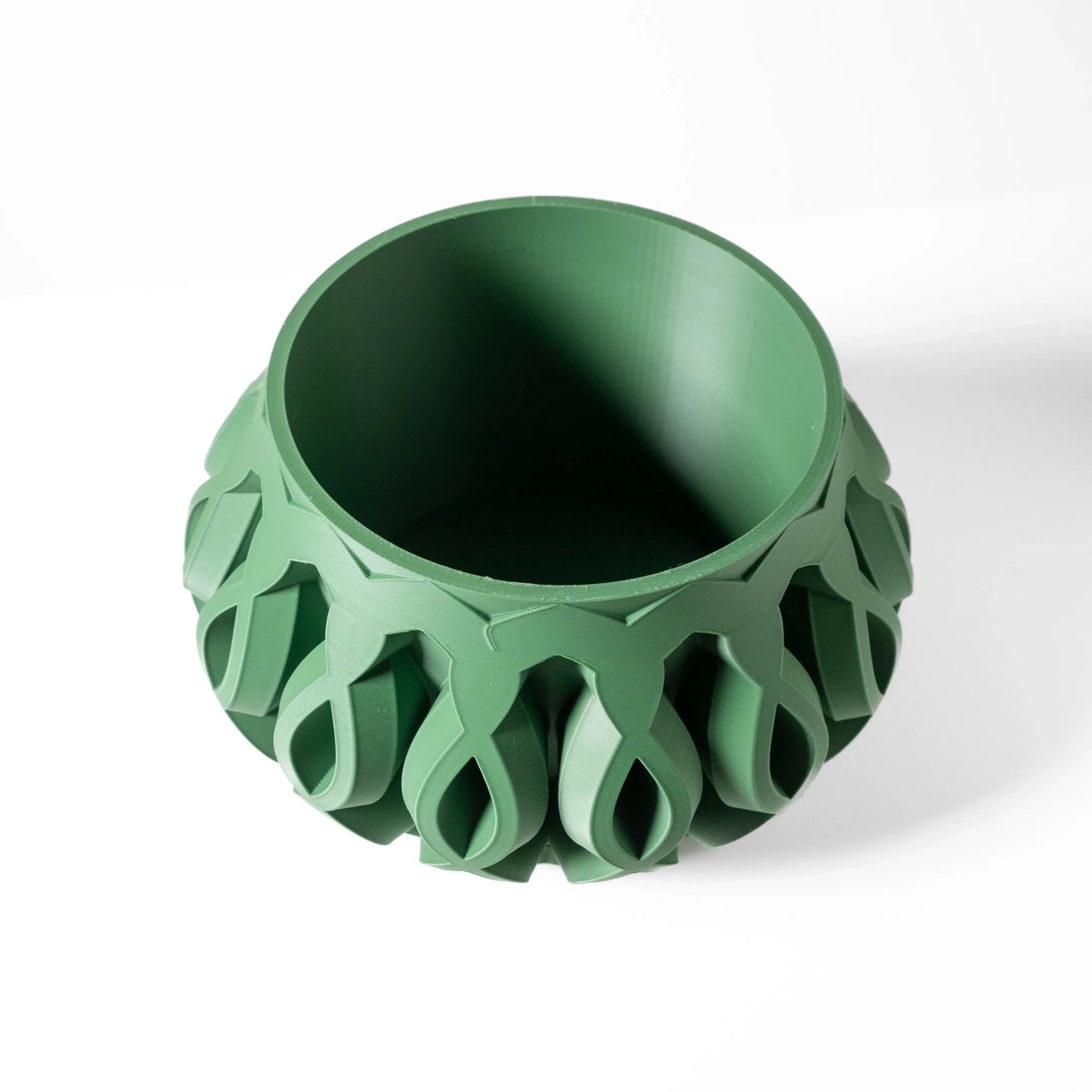 Pot décoratif vert mousse en matériau moderne, forme ronde avec motifs géométriques évidés sur la paroi extérieure.