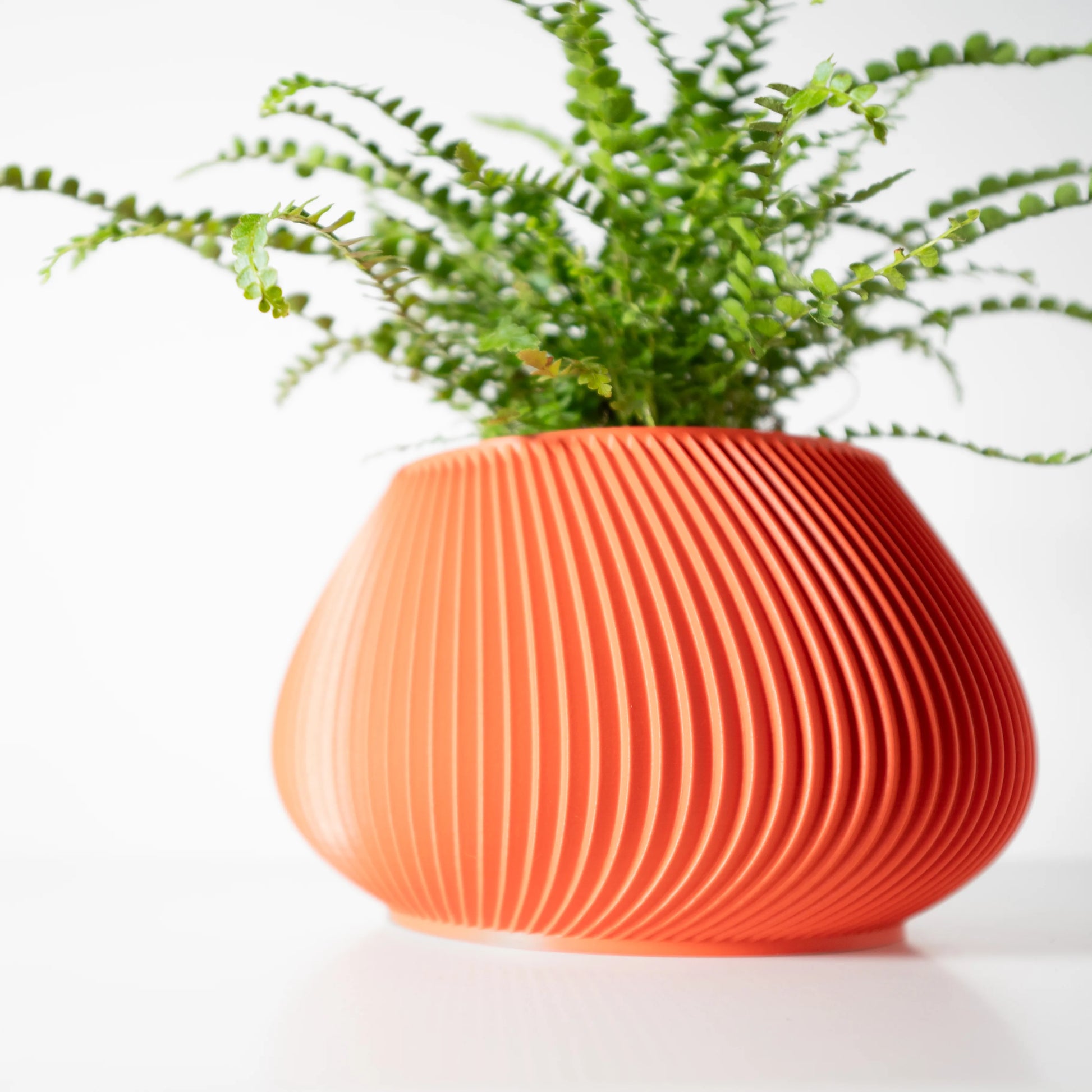 Pot décoratif orange en matériau moderne, forme arrondie avec rainures verticales, plante verte dedans.