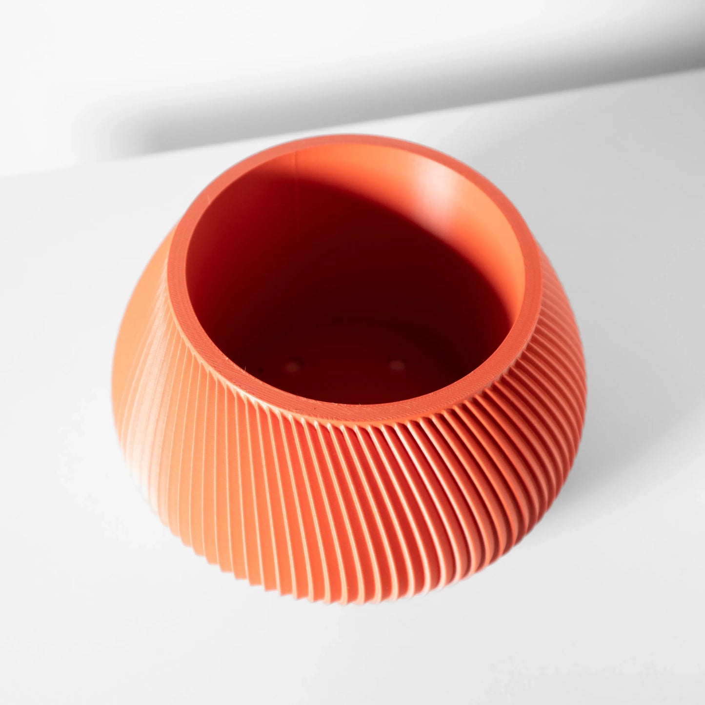 Pot décoratif rond en plastique orange vif avec surface nervurée verticale et intérieur lisse creux.