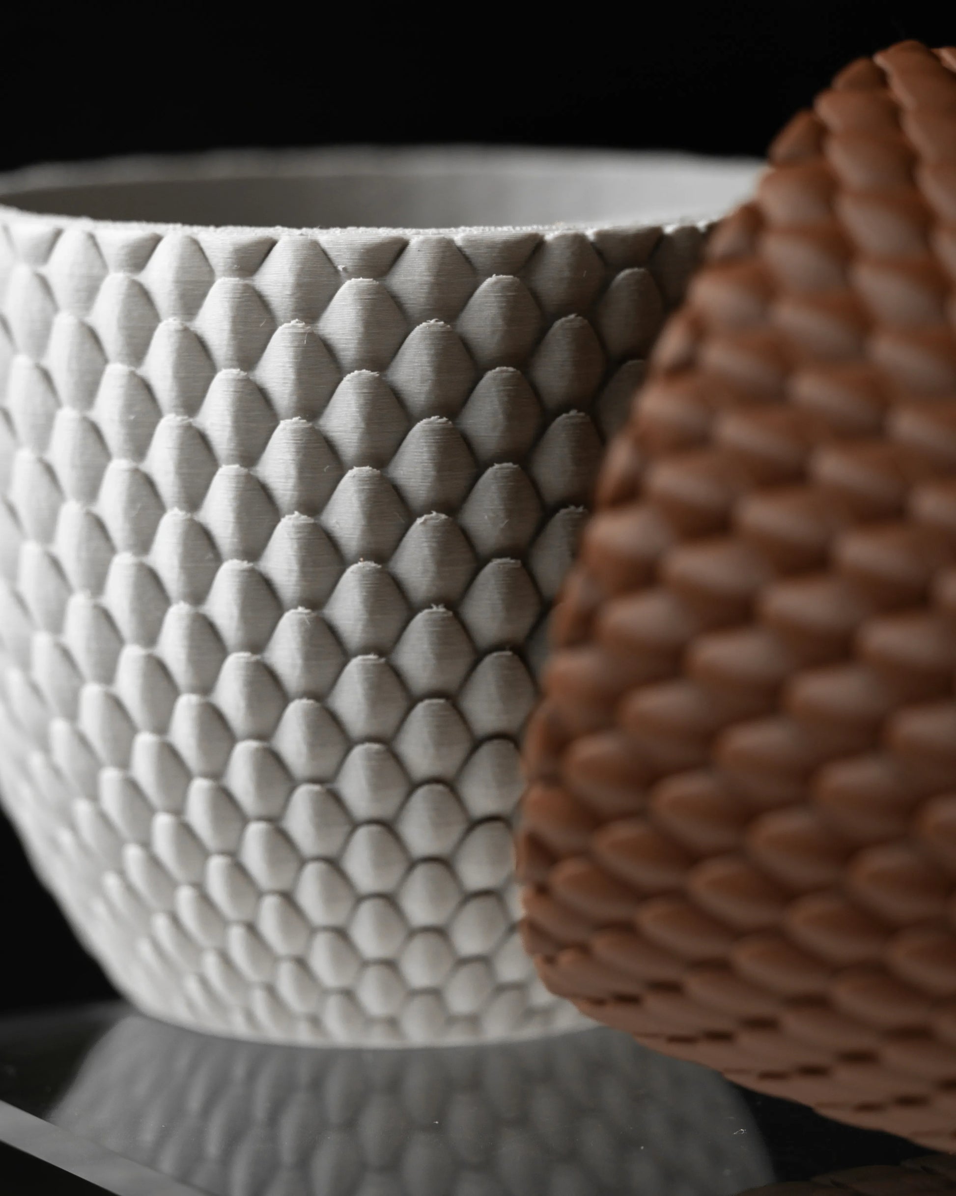 Pot décoratif blanc avec texture en relief imitant des écailles, finition mate, forme arrondie, posé à côté d’un pot marron.