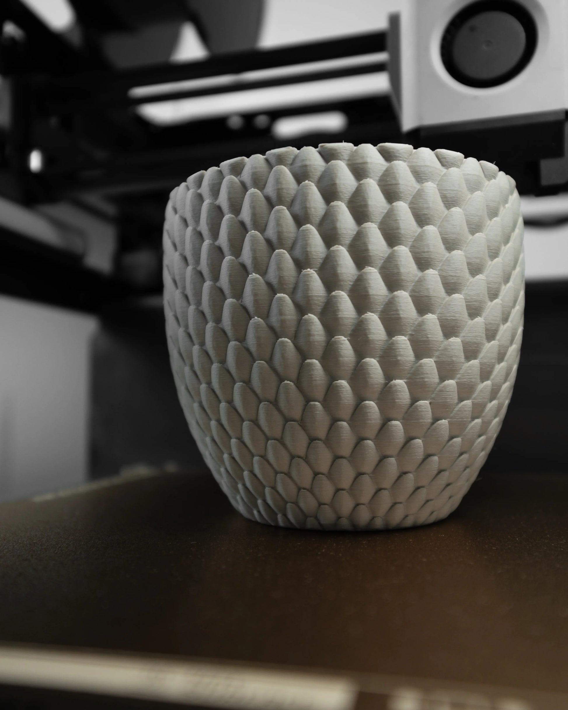 Pot décoratif gris clair avec texture en écailles de dragon en relief, forme arrondie et materiau texturé mat, posé sur un.