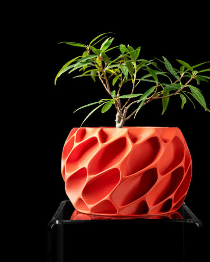 Pot décoratif rouge en plastique avec surface texturée en relief ondulé, forme ronde et plante verte à fines feuilles pâles.