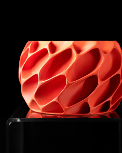 Pot décoratif rouge vif avec surface ajourée en motifs organiques en relief, forme ronde et contemporaine.