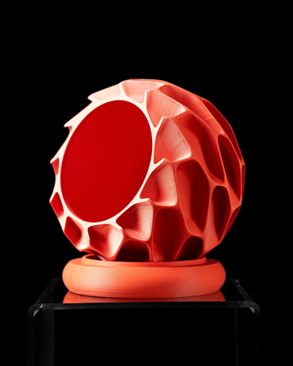 Pot décoratif rouge vif avec texture géométrique en relief, forme sphérique ajourée, posé sur un socle rond assorti.