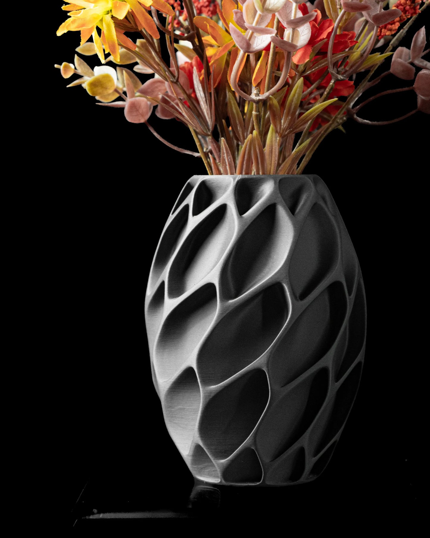 Vase noir mat design moderne avec motifs organiques en relief, forme ovoïde, contenant des fleurs séchées colorées.