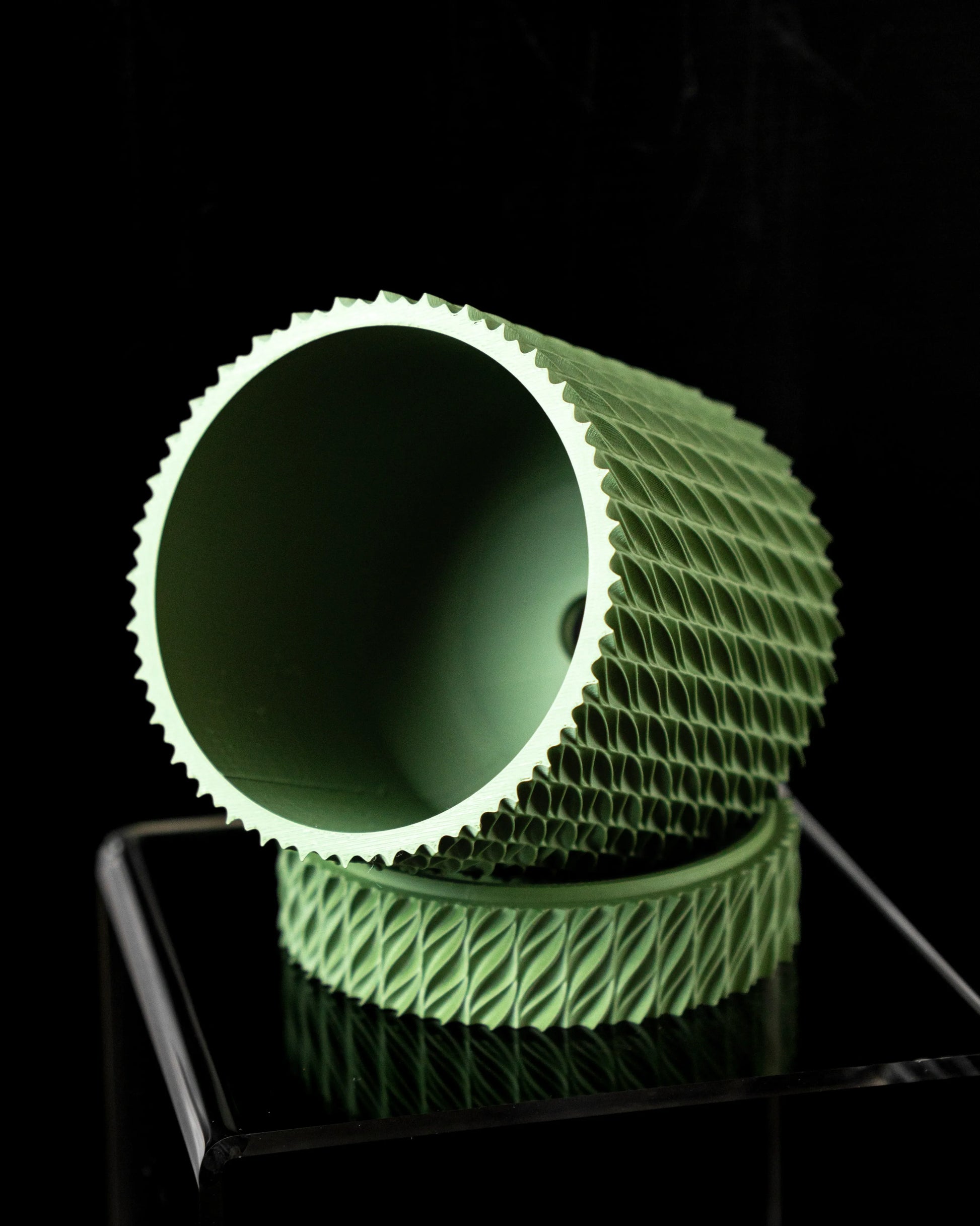 Pot décoratif vert clair cylindrique incliné, surface extérieure texturée en relief géométrique, intérieur lisse, posé sur.