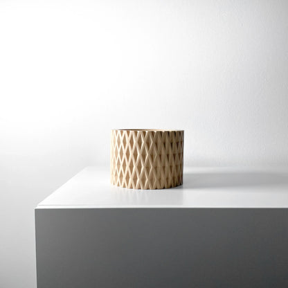 Pot cylindrique beige avec motif géométrique en relief ajouré, style moderne, posé sur un coin blanc minimaliste.