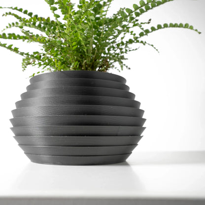 Pot décoratif rond noir mat avec rainures horizontales, style moderne et épuré, plante verte à petites feuilles.
