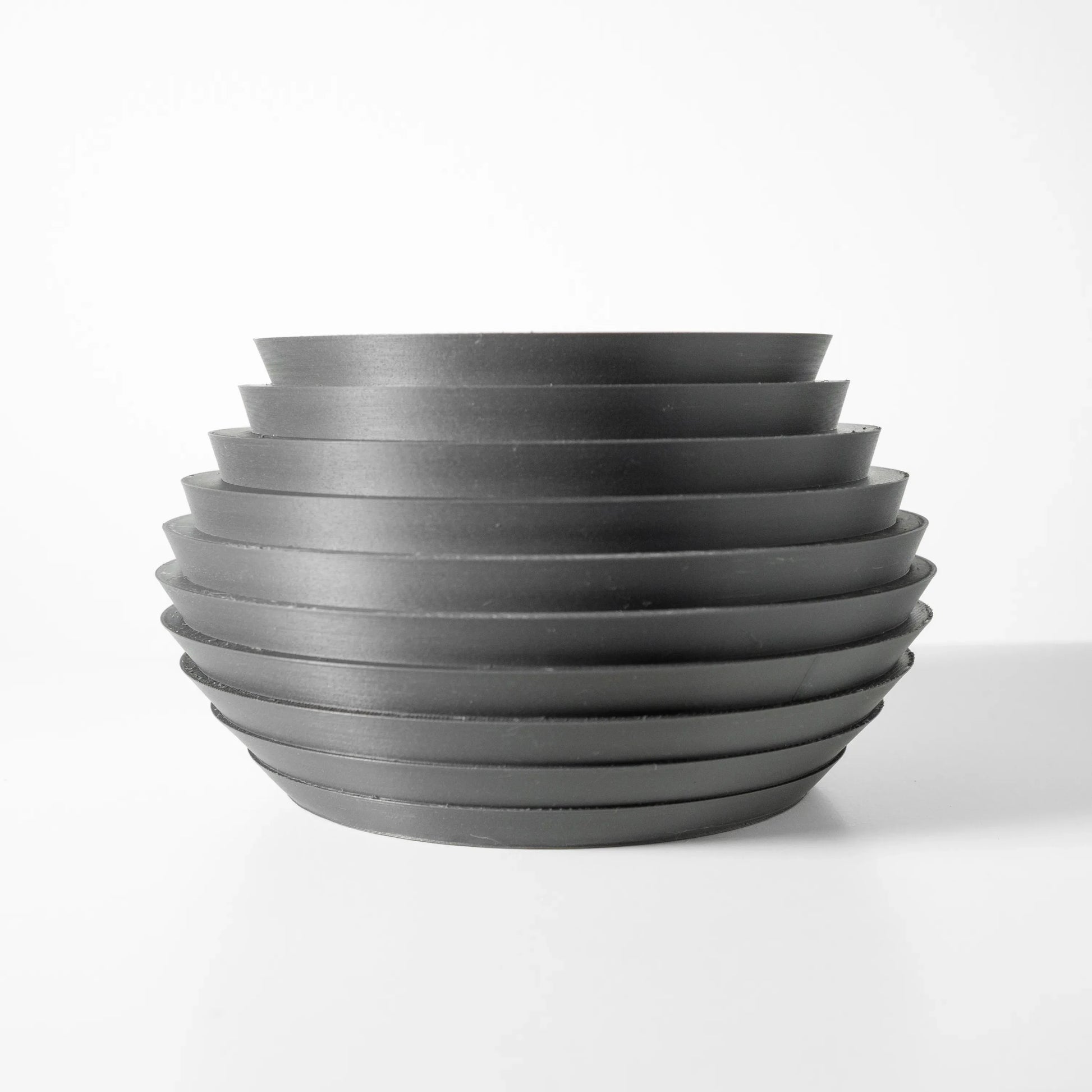 Pot décoratif moderne en métal gris foncé avec surface nervurée en cercles horizontaux superposés, forme arrondie et large.
