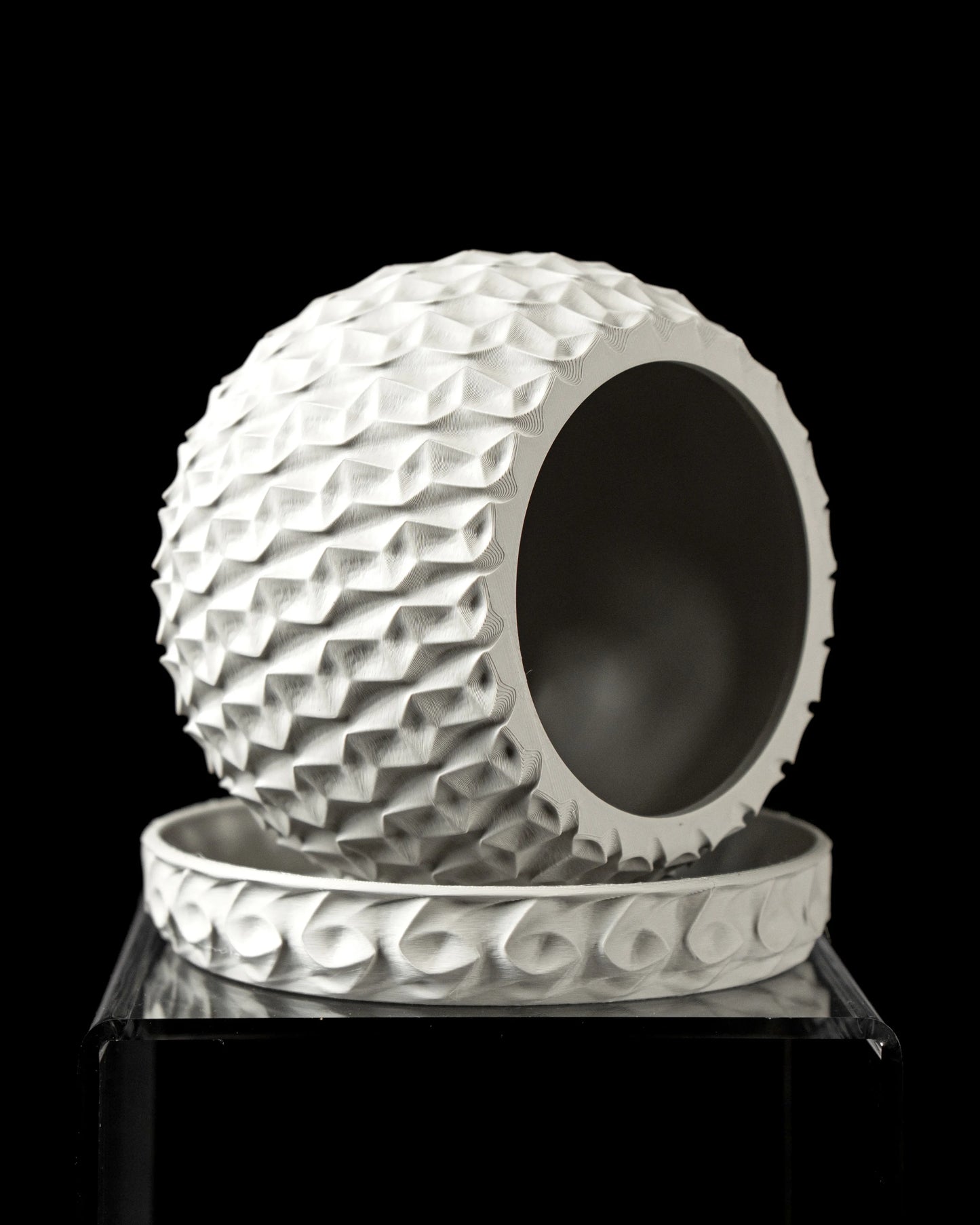 Pot décoratif blanc sphérique à surface hexagonale en relief, ouvert sur un côté, posé sur un socle assorti rond avec motifs