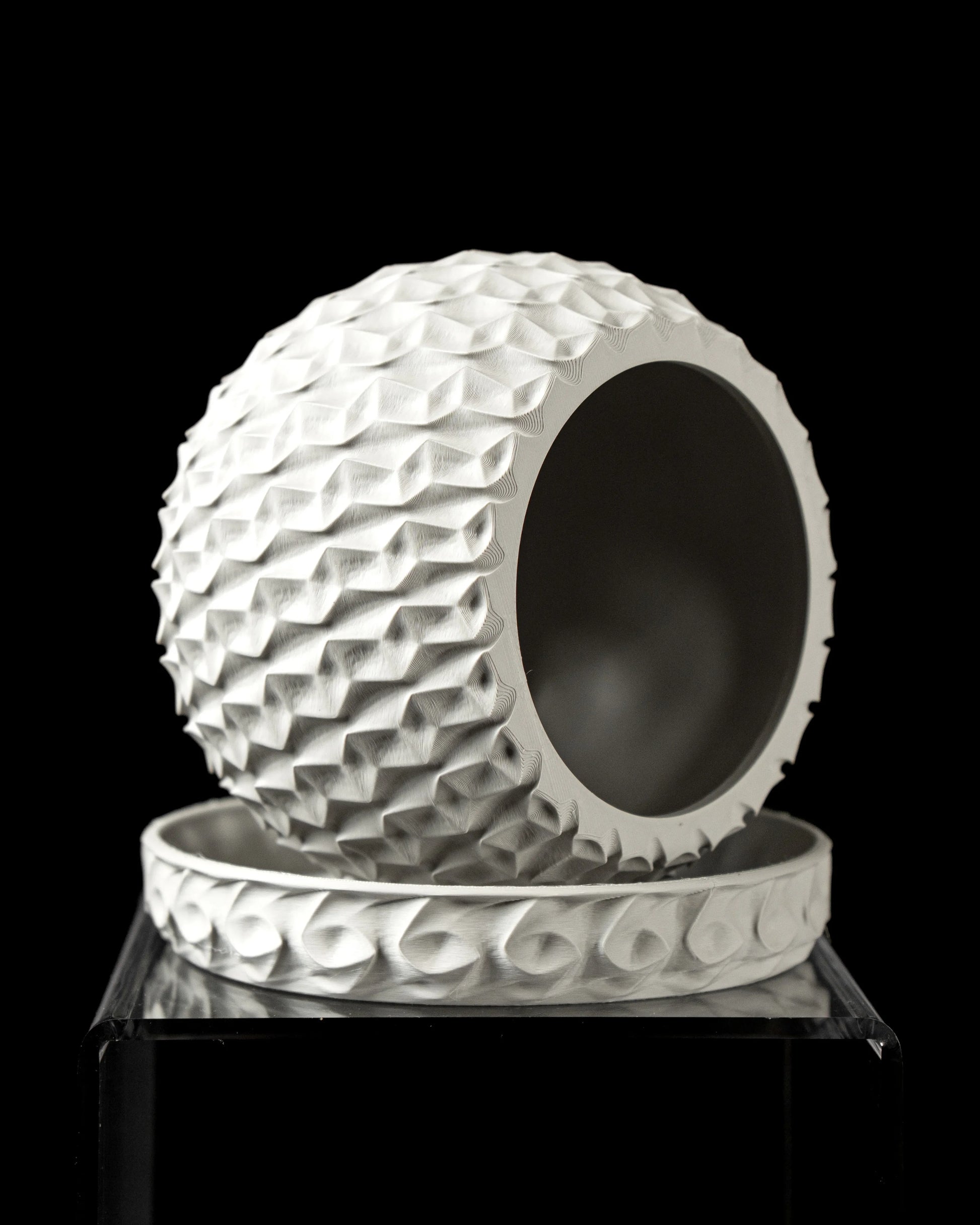 Pot décoratif blanc sphérique à surface hexagonale en relief, ouvert sur un côté, posé sur un socle assorti rond avec motifs