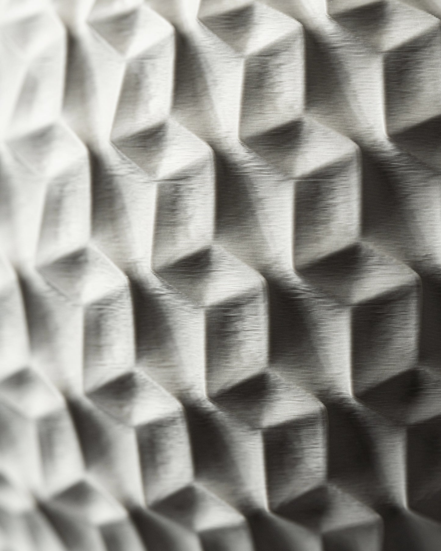 Pot décoratif hexagonal en gris clair avec motifs géométriques en relief, finition mate et texturée, surface angulaire.