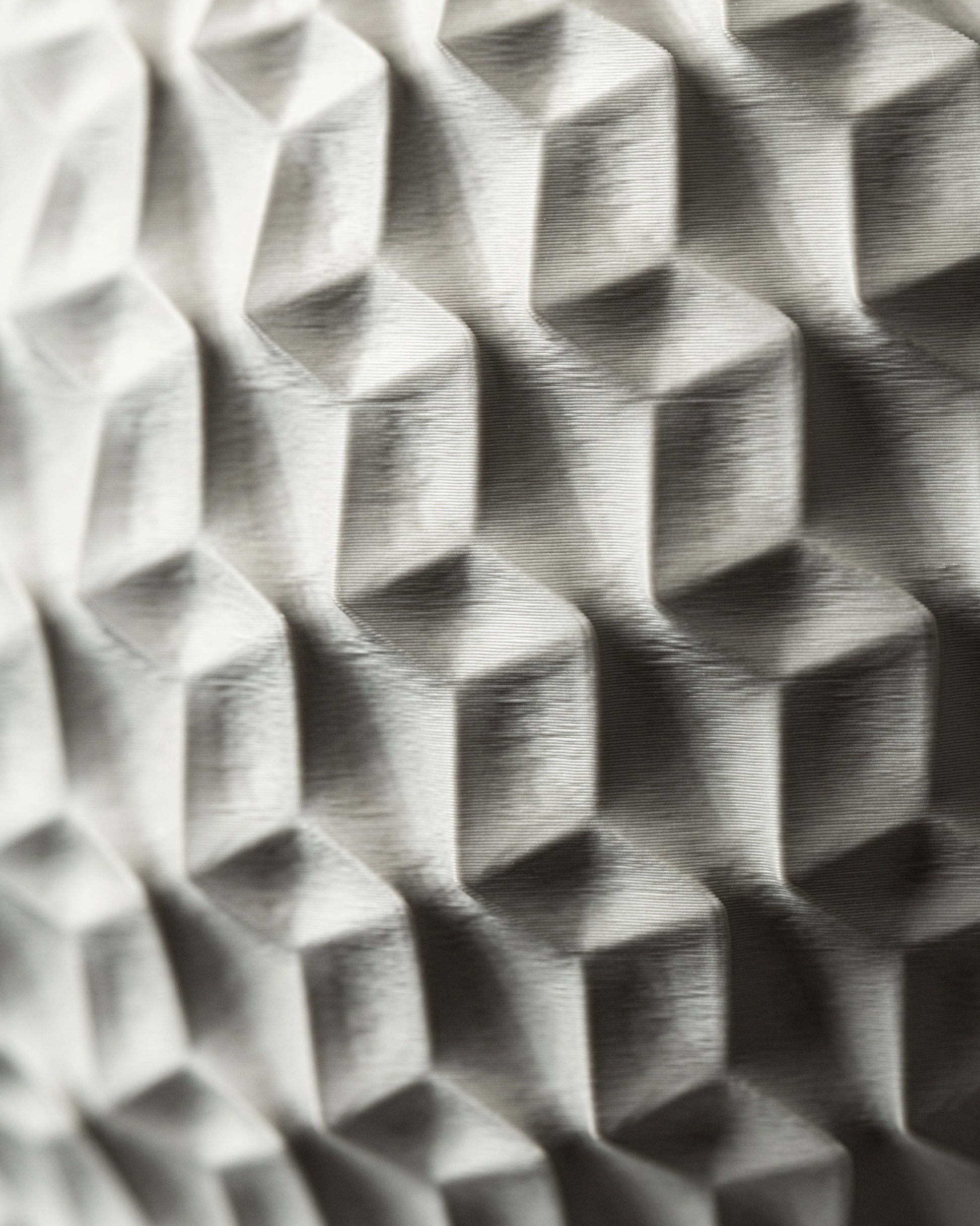 Pot décoratif hexagonal en gris clair avec motifs géométriques en relief, finition mate et texturée, surface angulaire.