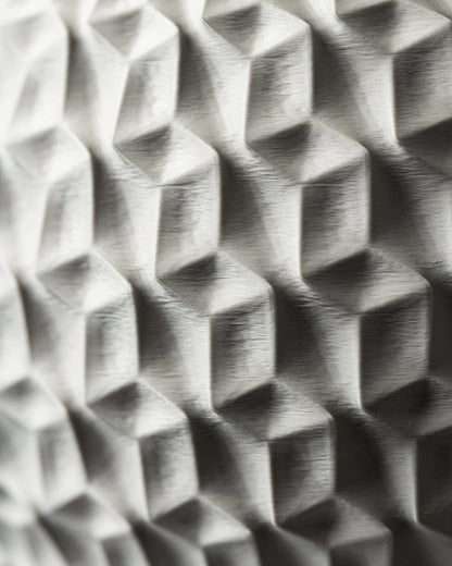 Pot décoratif hexagonal en gris clair avec motifs géométriques en relief, finition mate et texturée, surface angulaire.