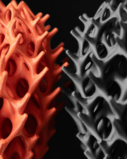 Deux vases aux formes ondulées et perforées, l’un orange vif et l’autre gris foncé, style moderne et organique, surface.