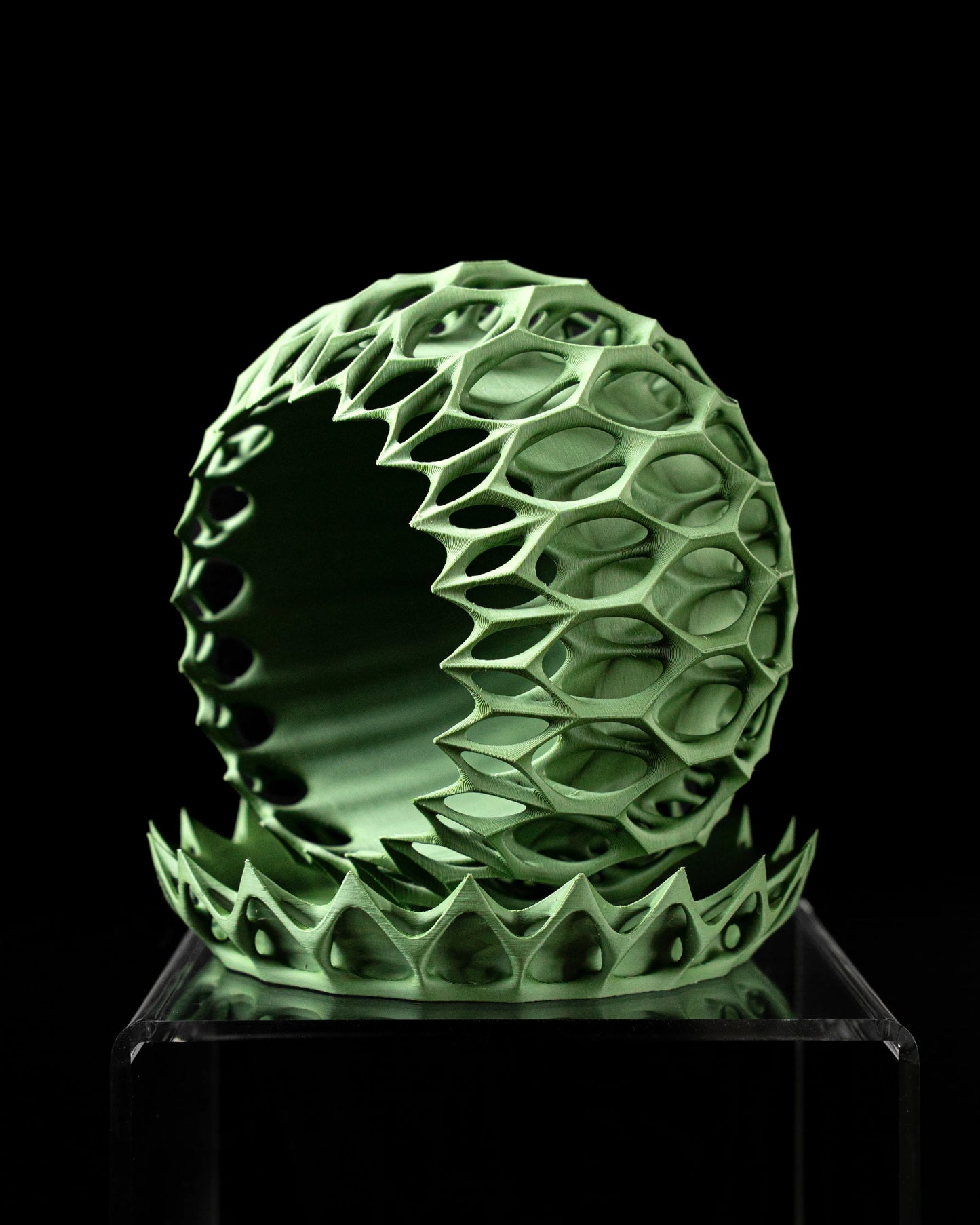 Pot décoratif vert clair en forme sphérique avec motif alvéolé tridimensionnel ajouré, posé sur un socle assorti.