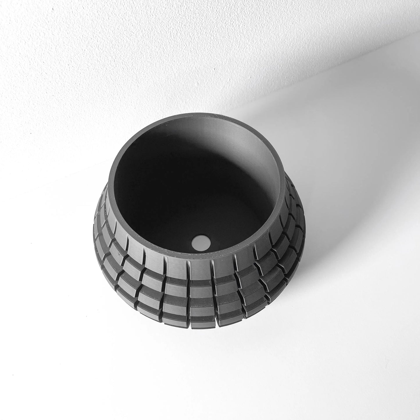 Pot décoratif noir en matière moderne avec surface texturée en carreaux réguliers et trou de drainage central.