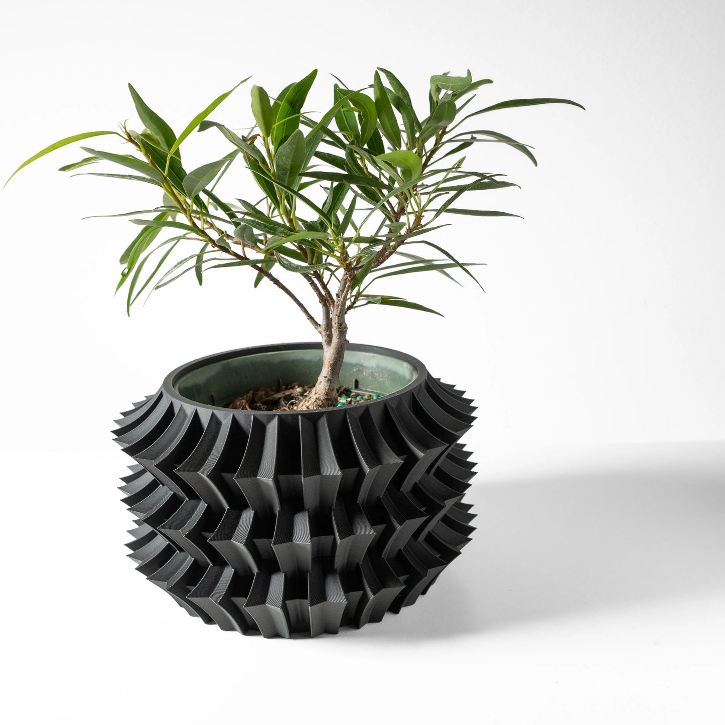Pot décoratif noir en plastique moderne avec motif géométrique tridimensionnel, accueillant une plante verte à feuilles.